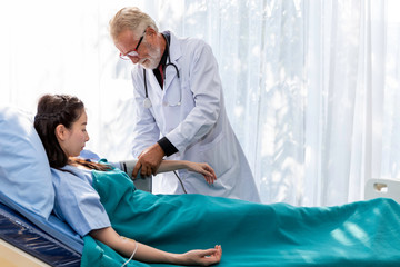 Senior Caucasian professional doctor man check blood pressure with Asian woman patient in the...