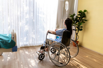 Asian woman patient sitting in the wheelchair at hospital room.