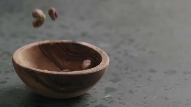 Slow motion peeled pistachios falls into olive bowl on terrazzo surface