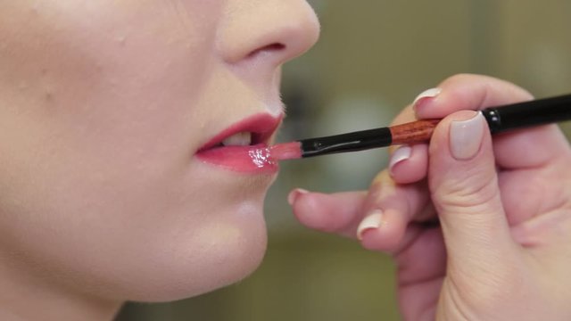 Professional make-up artist applying lip gloss on client s lips with a brush.