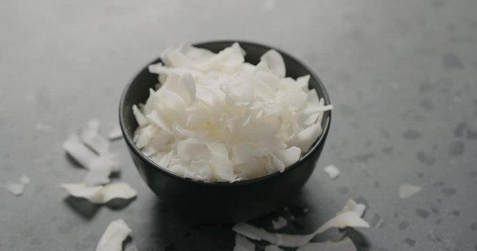 Handheld slow motion of coconut chips in black bowl on terrazzo surface