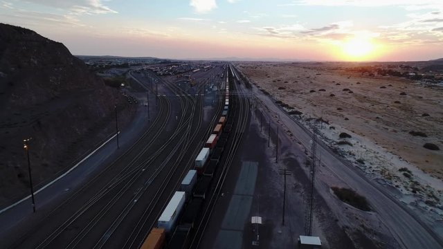 Aerial over railway yard following coal frieght train, at sunset in California