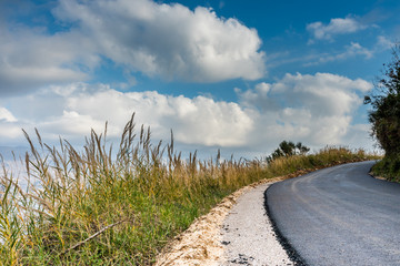 Mountain road from a low angle with a right hand bend in the distance, set against a blue sky with...