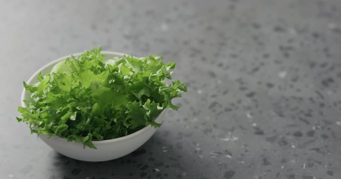 Handheld slow motion of frisee leaves in white bowl on terrazzo surface