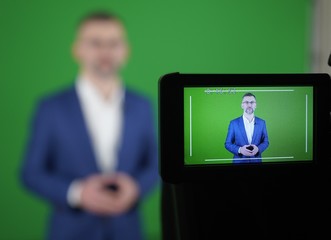 A blogger is recording a video on a green background.  The camcorder is recording a blogger.