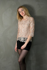 Portrait of a pretty cute smiling young blonde woman with minimal makeup in a beige blouse on a gray background. It stands directly opposite the camera in various poses.