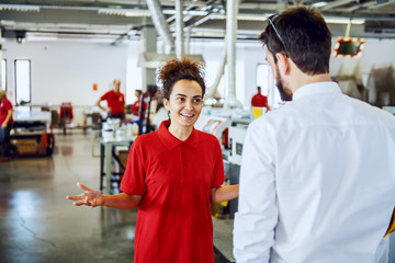 Obraz premium Smiling caucasian female employee with curly hair talking to her director while standing in printing shop.