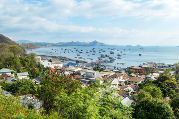 Fototapeta premium Widok na port ze szczytu wzgórza w Labuan Bajo, Flores, Indonezja. Do jego brzegu zakotwiczonych jest wiele łodzi. Z tyłu jest kilka wysp. Małe miasto z przodu. Szczęście i piękno