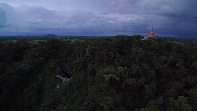 VDO. Aerial view of Golden pagoda on top hill with thunder and rainy sky background, sunset with rain at Wat Khao Chong Pran (Bat Temple), Ratchaburi, Thailand.