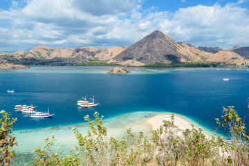 Naklejka premium View from top of a cliff on Kelor Island, Komodo, Indonesia. Island is surrounded with white sand beaches and turquoise water. There is another island in the back.There are boats anchored to a shore.