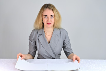 Model Sits at a table directly opposite the camera in various poses. Portrait of a pretty cute smiling young blonde business woman with minimal makeup in a gray suit on a white background.