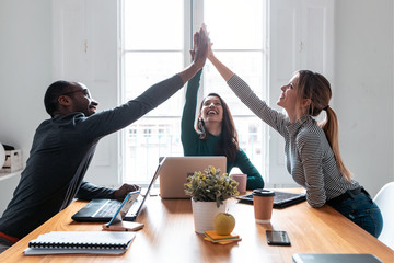 Group of successful young businesspeople holding up their right hands on coworking place.