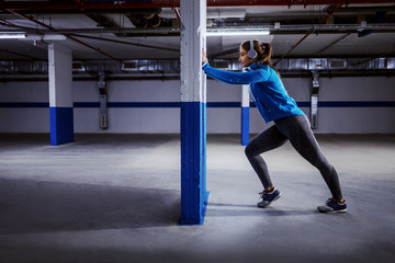 Young fit attractive caucasian sportswoman in tracksuit running fast in garage. Urban life concept.