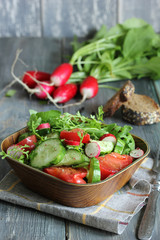 The concept of healthy kitchen. Salad of fresh herbs, radish, cucumber and tomatoes with oil on a lignt wooden background. Copy space, background image.