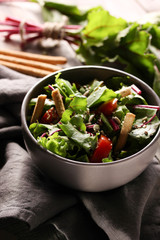 The concept of live kitchen. Salad of fresh beet tops and tomatoes with olive oil on a light wooden background. Copy space, background image.