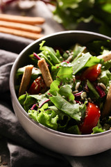 The concept of live kitchen. Salad of fresh beet tops and tomatoes with olive oil on a light wooden background. Copy space, background image.