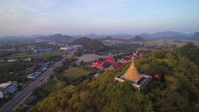 VDO. Aerial view of golden pagoda on top hill and buddhist temple with cloudy sky background, Wat Khao Chong Pran (Bat Temple), Photharam, Ratchaburi, Thailand.