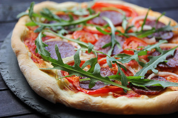 Italian cuisine concept, pizza pepperoni with sausage and arugula on a dark wooden background