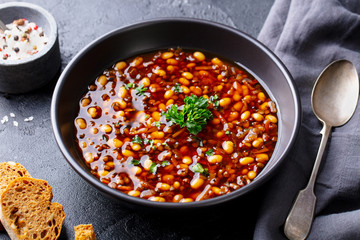 Bean soup in a black bowl. Dark background. Close up.