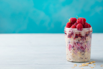 Overnight oats, bircher muesli with fresh raspberries in a glass jars on wooden table. Copy space.
