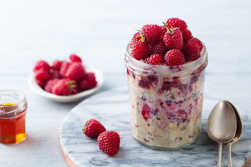Overnight oats, bircher muesli with fresh raspberries in a glass jars. Marble cutting board. Close...
