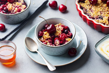 Cherry, red berry crumble in bowl. Grey stone background. Close up.