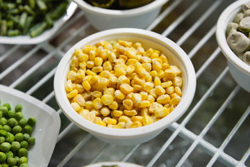 Frozen corn seeds lies in a white cup. Next to the plates are other frozen vegetables and fruits.