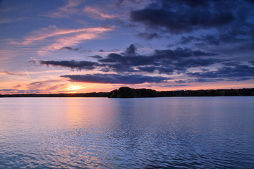 View of the lake at sunset with picturesque play of colors, silhouettes and a peaceful atmosphere.