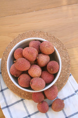 Fresh ripe litchi or lychee fruits in a bowl on wooden background. Litchi chinensis fruit on table