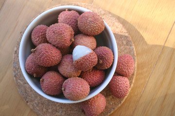 Fresh ripe litchi or lychee fruits in a bowl on wooden background. Litchi chinensis fruit on table