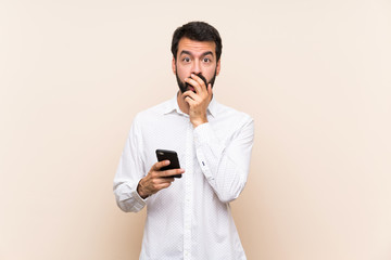 Young man with beard holding a mobile surprised and shocked while looking right
