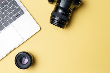 Photographer's workplace on a yellow background. Modern laptop, digital camera, lens, battery, smartphone. Minimalism. Top view. Copy space. Equipment for the photographer. The concept of freelancing