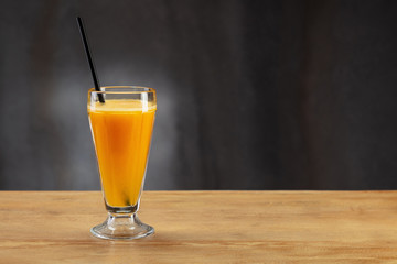 Fresh orange juice in glass with black straw on wooden background.