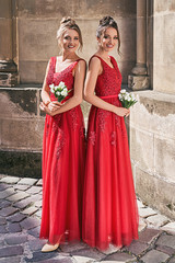 Two beautiful bridesmaids girls blonde and brunette ladies wearing elegant full length red chiffon...