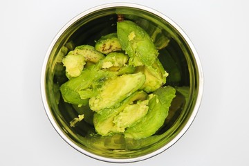 Close up of isolated metal bowl with cut avocado flesh slices, white background