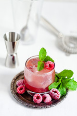 Delicious and refreshing cocktail for summer party. Raspberry syrup, soda, ice, pepper mint. Frozen berries as decor. Bartender equiment on background. Close up, white background
