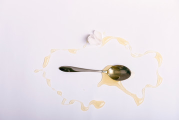 Metal spoon and pouring line of golden honey isolated on white.