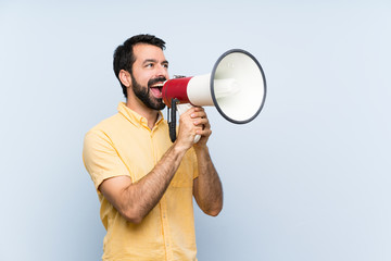 Young man with beard over isolated blue background shouting through a megaphone