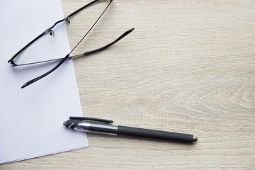 Flat Lay. Black pen, clean white office paper and black glasses on beige wooden background