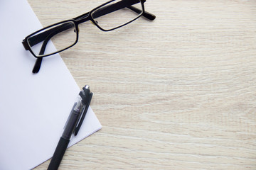 Flat Lay. Black pen, clean white office paper and black glasses on beige wooden background