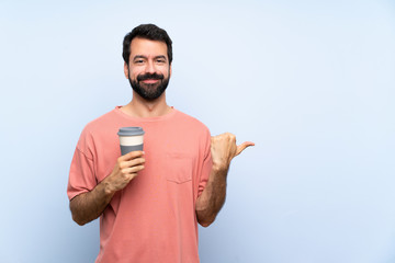 Young man with beard holding a take away coffee over isolated blue background pointing to the side to present a product