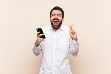 Young man with beard holding a mobile with fingers crossing