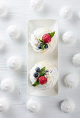 Dessert Pavlova with raspberries, blueberries and mint on a white table.