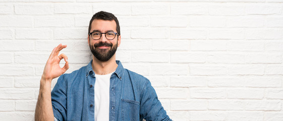 Obraz premium Handsome man with beard over white brick wall showing ok sign with fingers