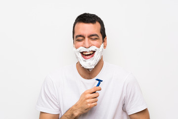 Man shaving his beard over isolated white background smiling a lot