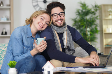 couple sitting on sofa drinking coffe or tea using laptop