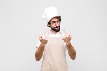 young crazy chef feeling provocative, aggressive and obscene, flipping the middle finger, with a...
