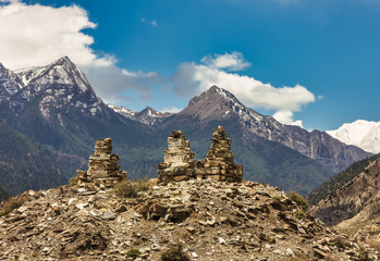 Three Buddhist stone stupas on top of a rocky cliff with a view of the snow covered Himalayan mountains in the village of Marpha on the Annapurna Circuit trekking trail in Nepal.