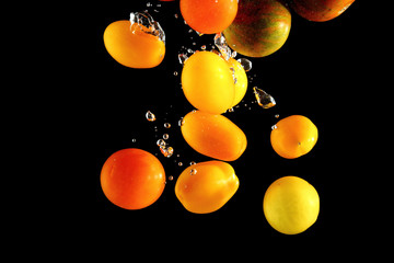 Different tomato cultivars falling into water at black background