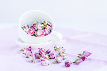 Selective focus on dried roses in a white cup at pink pastel  background. Copy space.